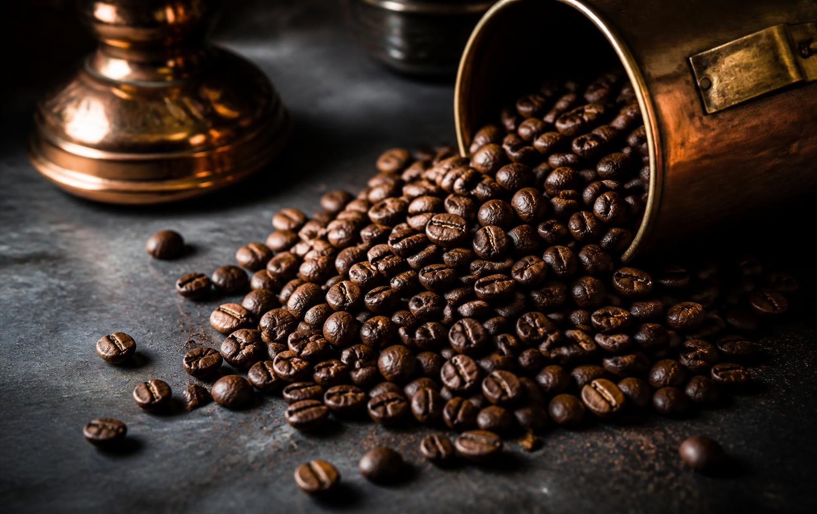 Roasted coffee beans on a dark surface lit with copper light